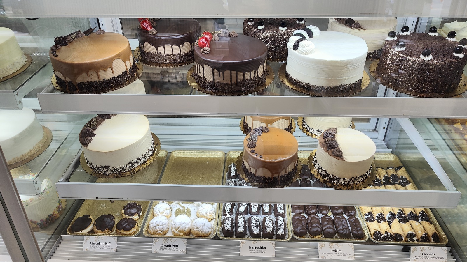 Whole cakes and cream pastries arranged in a refrigerated case at Classic Bakery