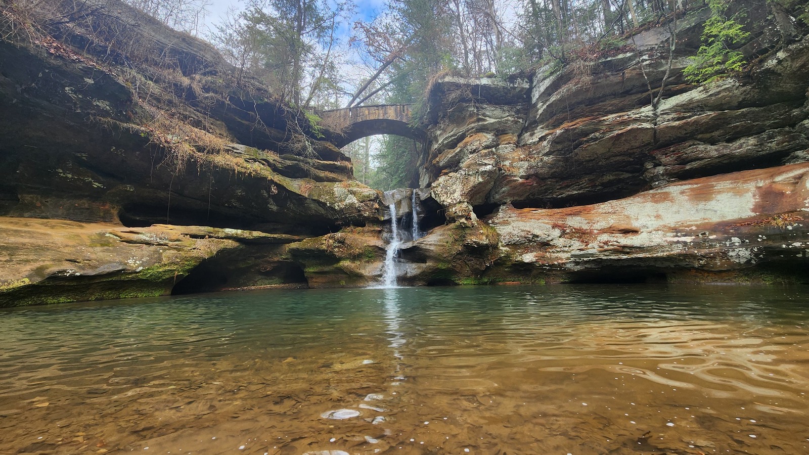 Stone bridge spanning a small waterfall above a clear pool in Hocking Hills State Park