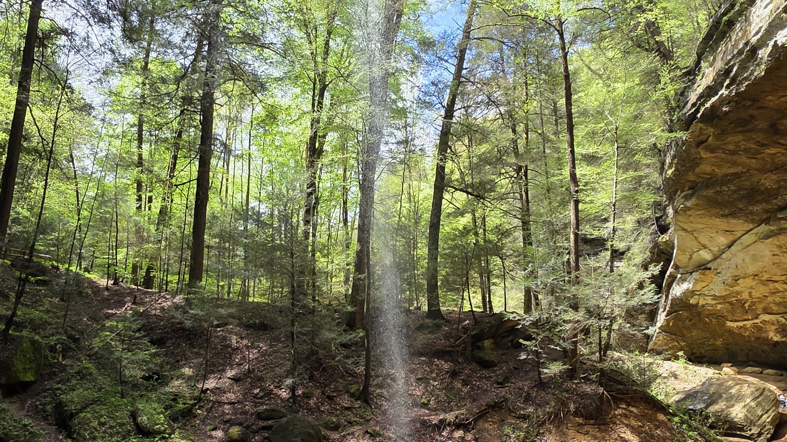 Thin waterfall dropping from the Ash Cave overhang into a sandy basin at Hocking Hills State Park