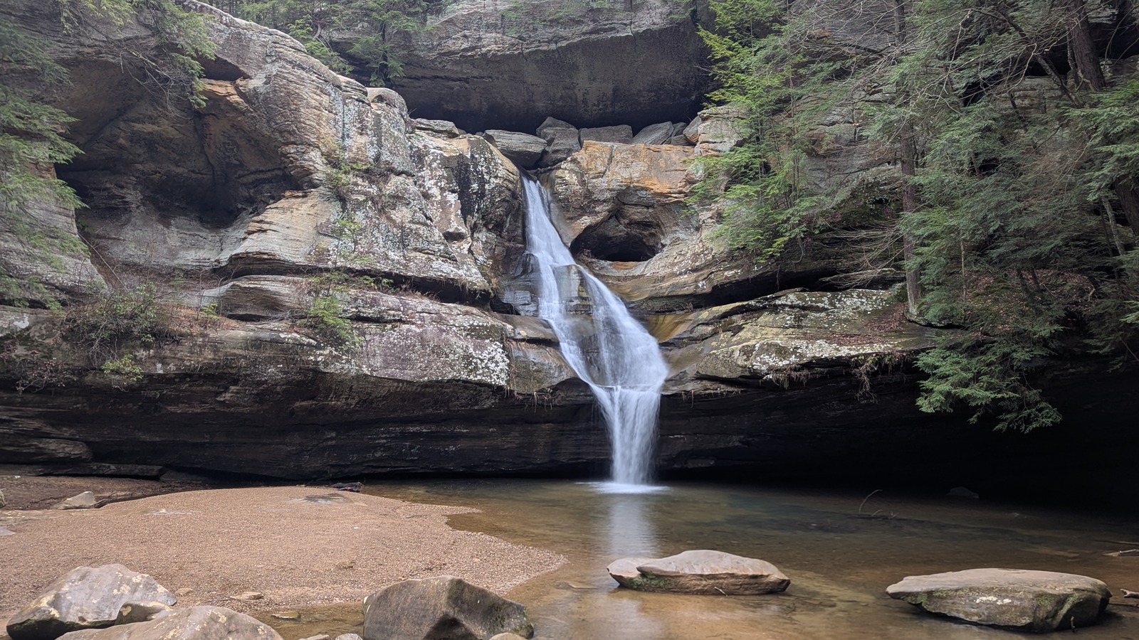 Cedar Falls dropping into a shallow pool framed by layered sandstone walls at Hocking Hills State Park