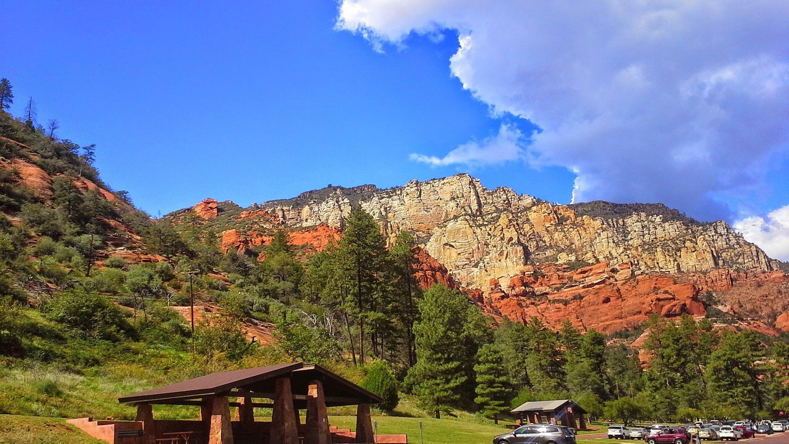 Slide Rock State Park sign with red cliffs and pine-covered slopes rising behind it