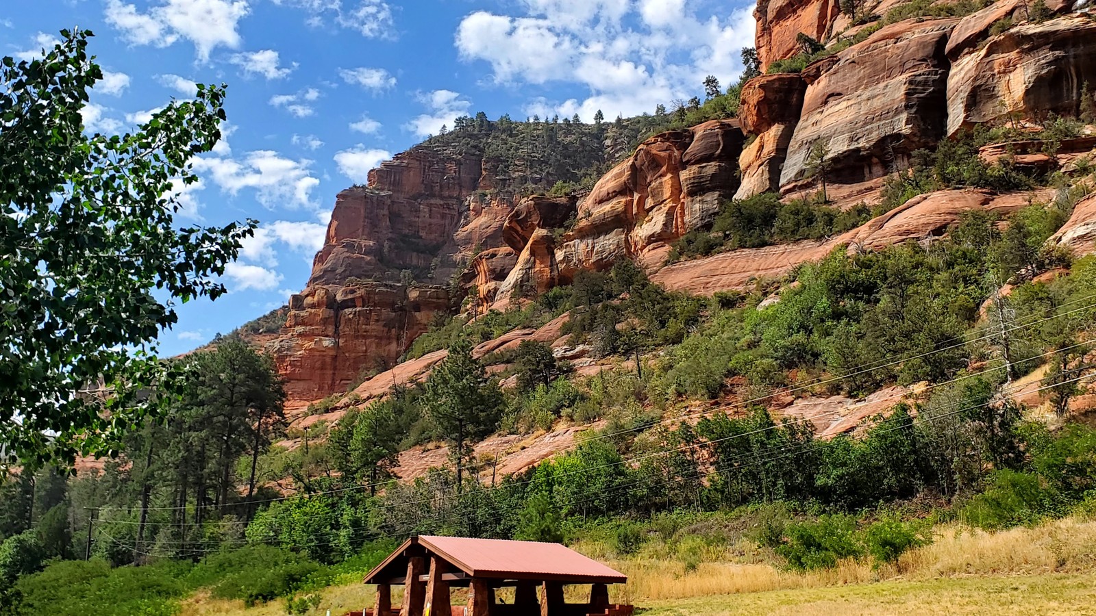 The historic apple packing shed and a small ramada beneath steep red cliffs at Slide Rock State Park