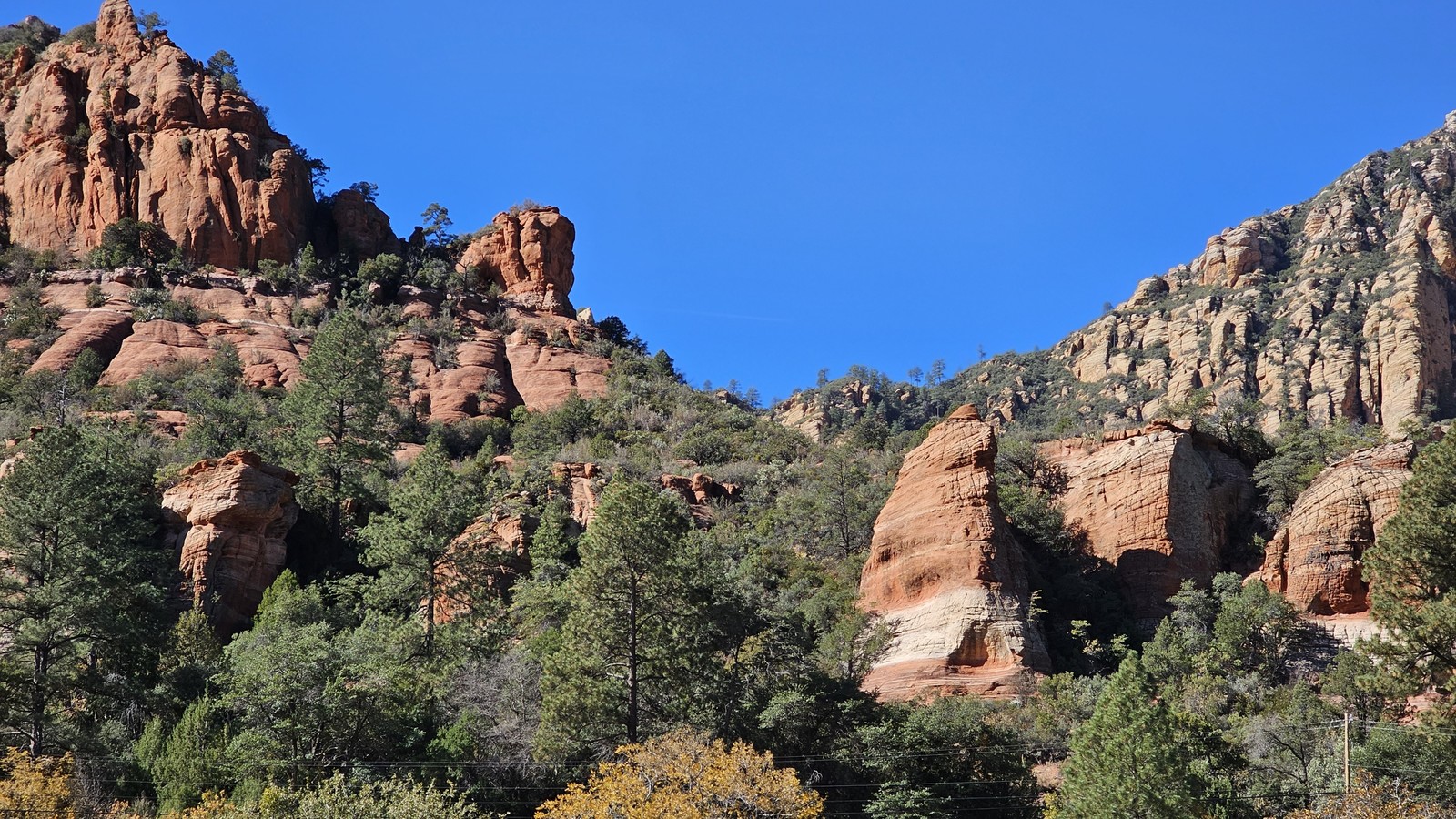 Apple orchard trees and scrubby hillside beneath towering red rocks at Slide Rock State Park