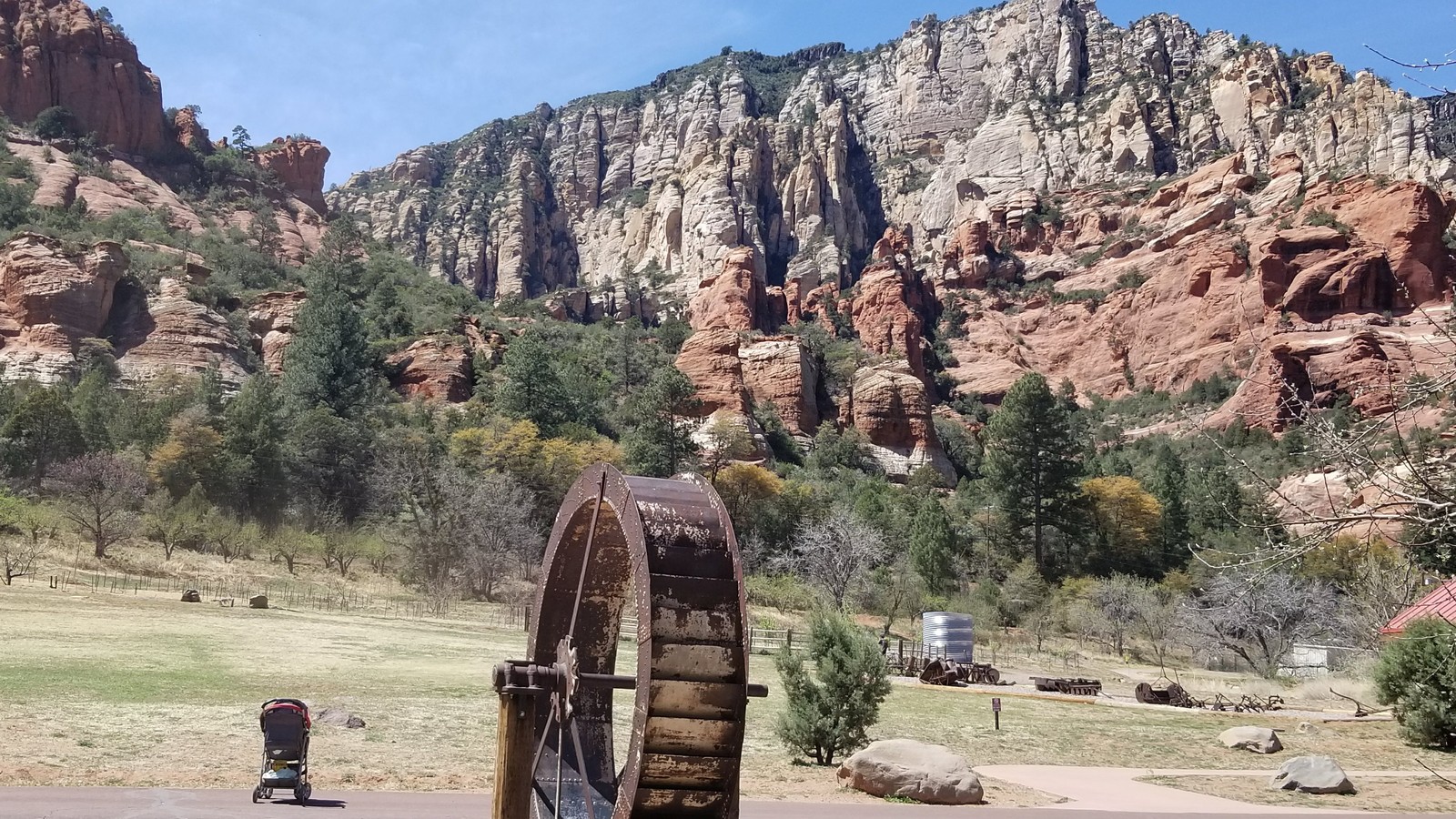 Historic water wheel and farm equipment in an open field below a pale canyon wall at Slide Rock State Park