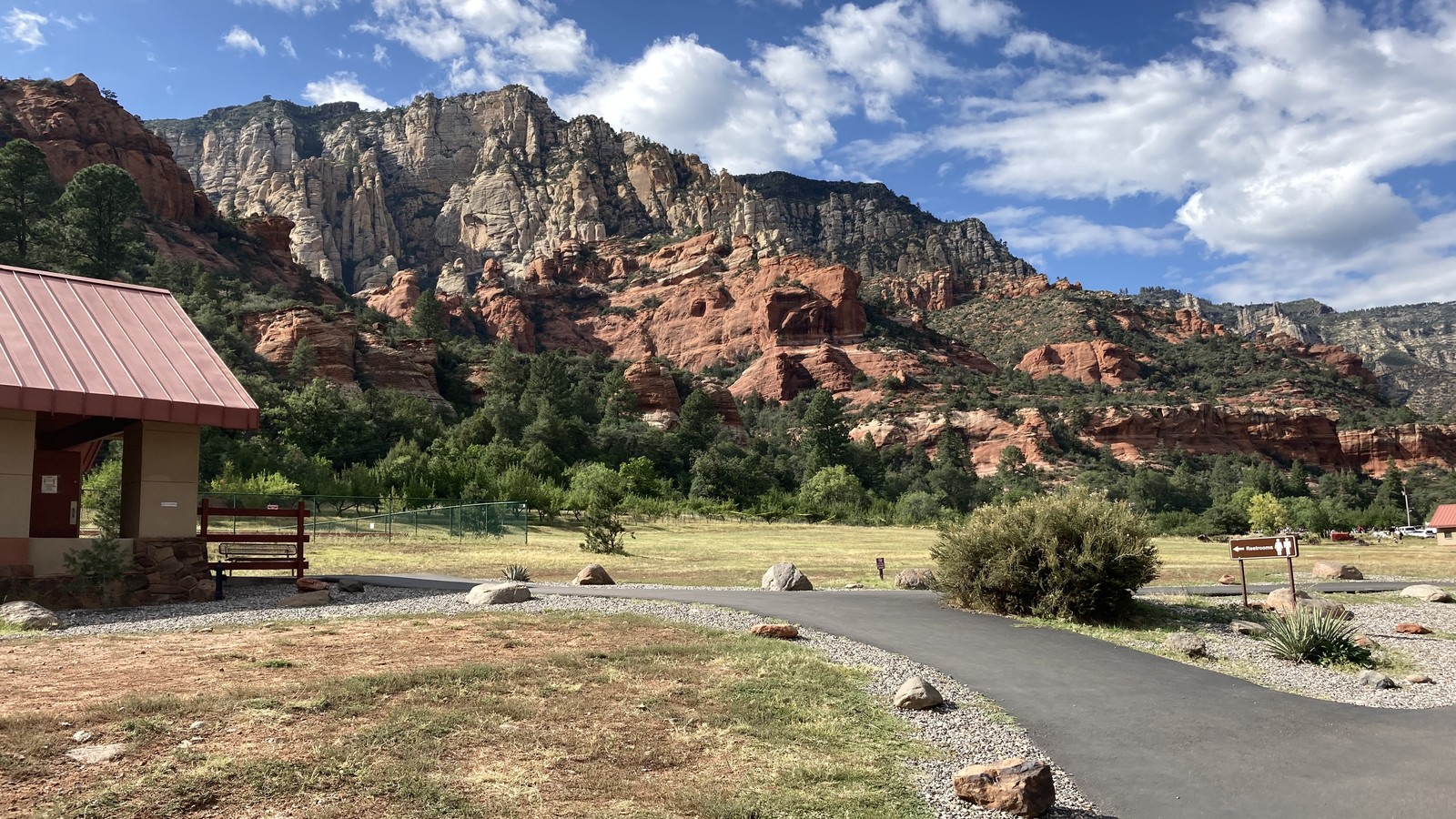 A curving paved picnic path with open lawn and dramatic cliffs at Slide Rock State Park