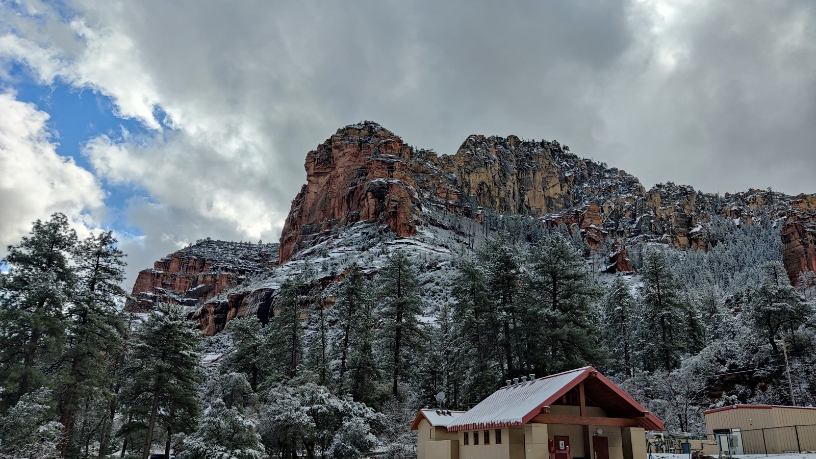 Snow-dusted red cliffs towering over a cabin roof at Slide Rock State Park