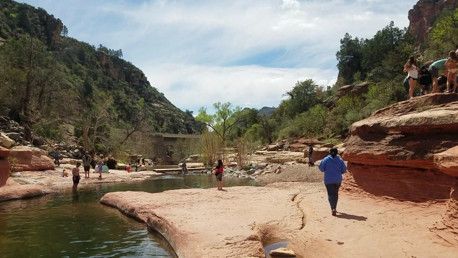 A sandstone creek route curving through Oak Creek Canyon with distant visitors and layered cliffs