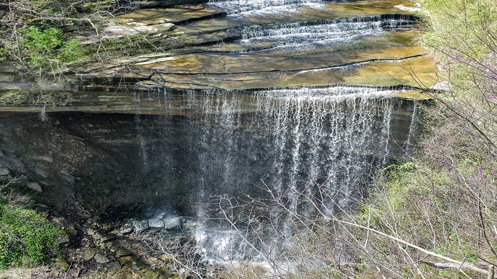 Wide waterfall curtain spilling beneath a layered rock shelf at Clifty Falls State Park.