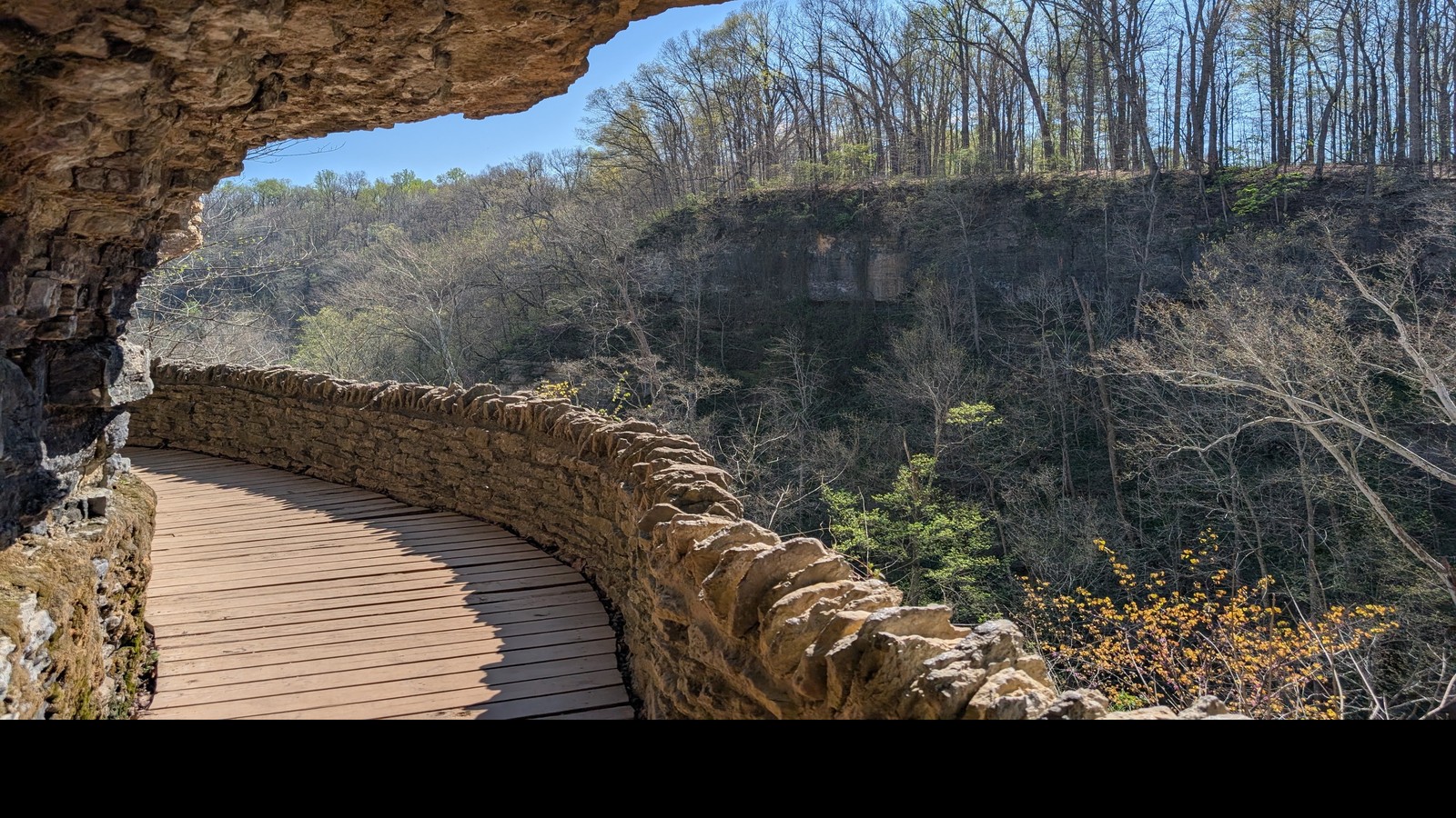 Stone-walled boardwalk curving beneath a cliff at Clifty Falls State Park.