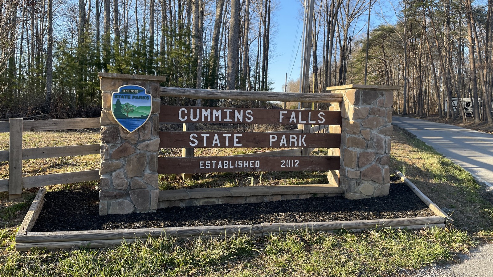 Stone entrance sign for Cummins Falls State Park beside the road.
