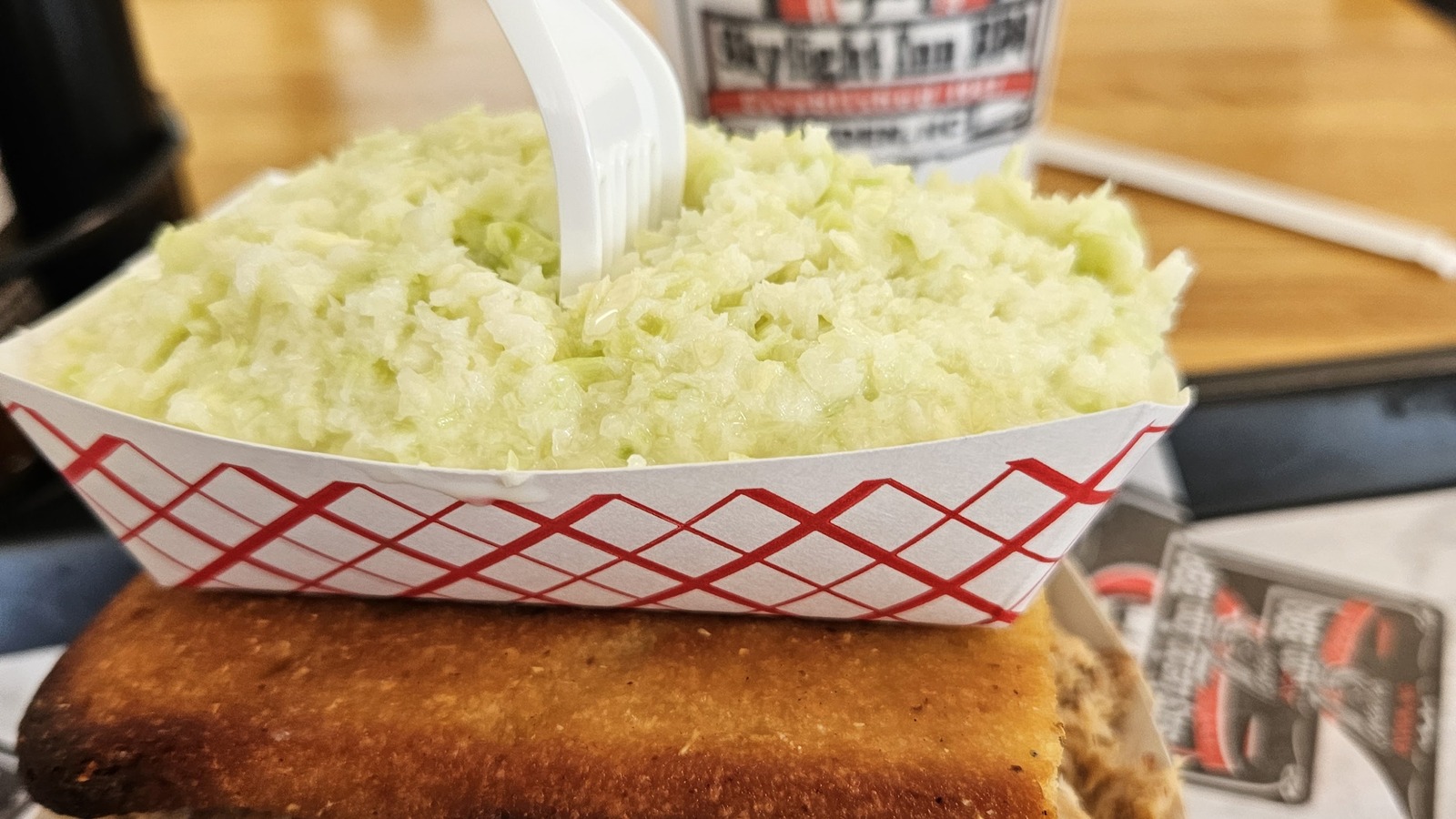 Paper tray filled with pale yellow slaw on a wooden table at Skylight Inn BBQ