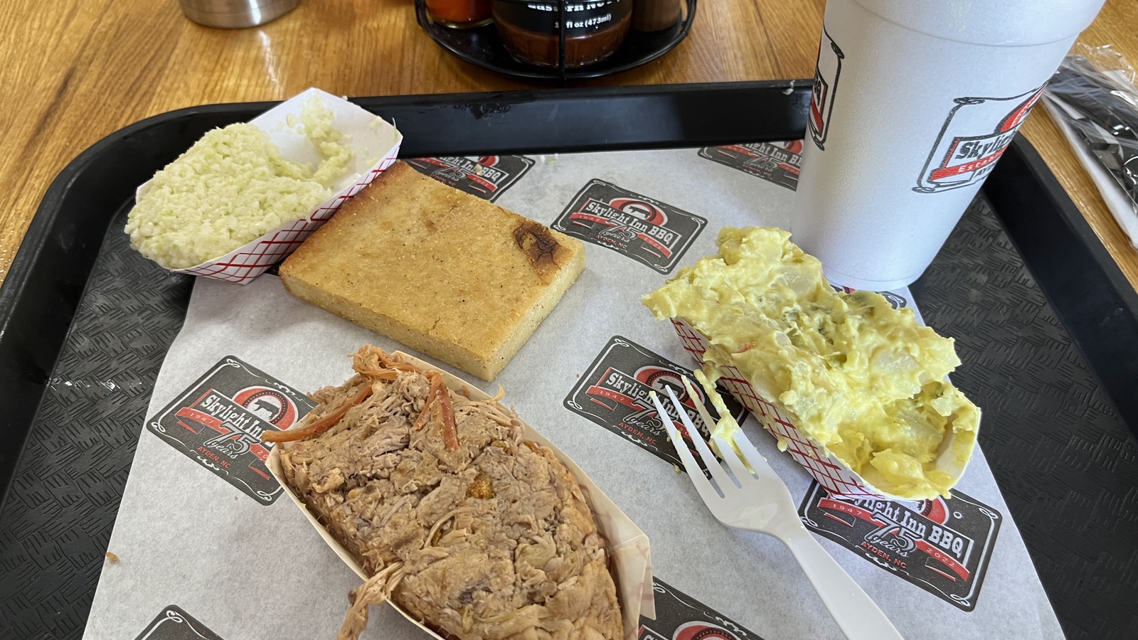 Barbecue tray with chopped pork, slaw, cornbread, cup, and bottled drink on the table