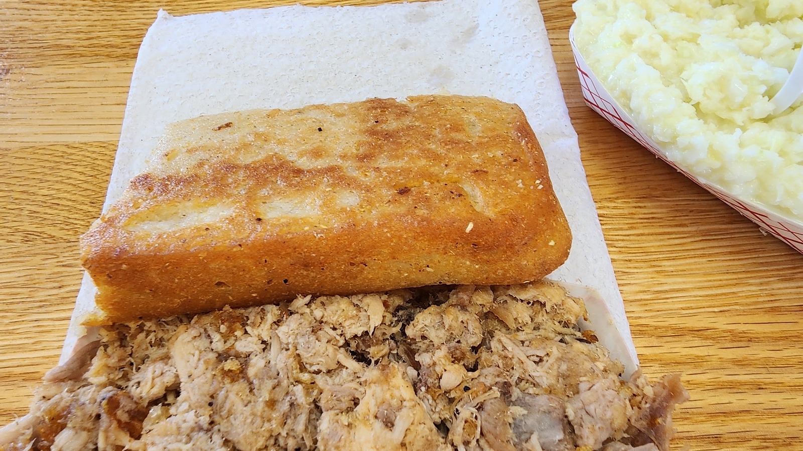 Golden square of cornbread resting over chopped pork beside a tray of slaw