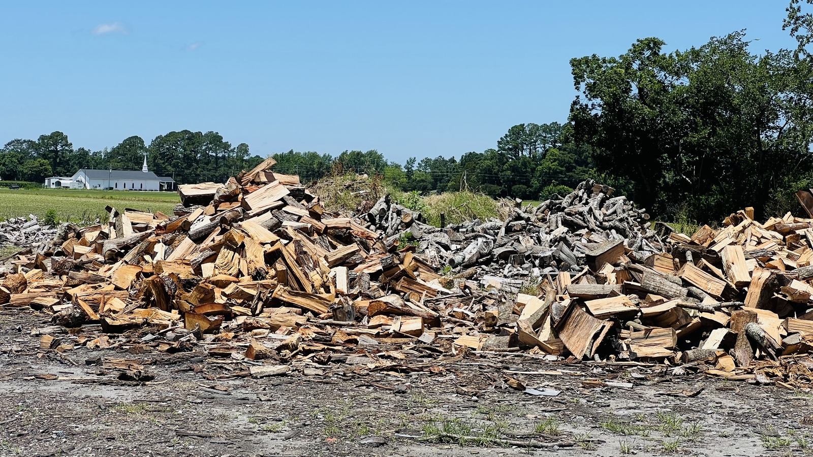 Tall stacks of split wood spread across the yard beside Skylight Inn BBQ
