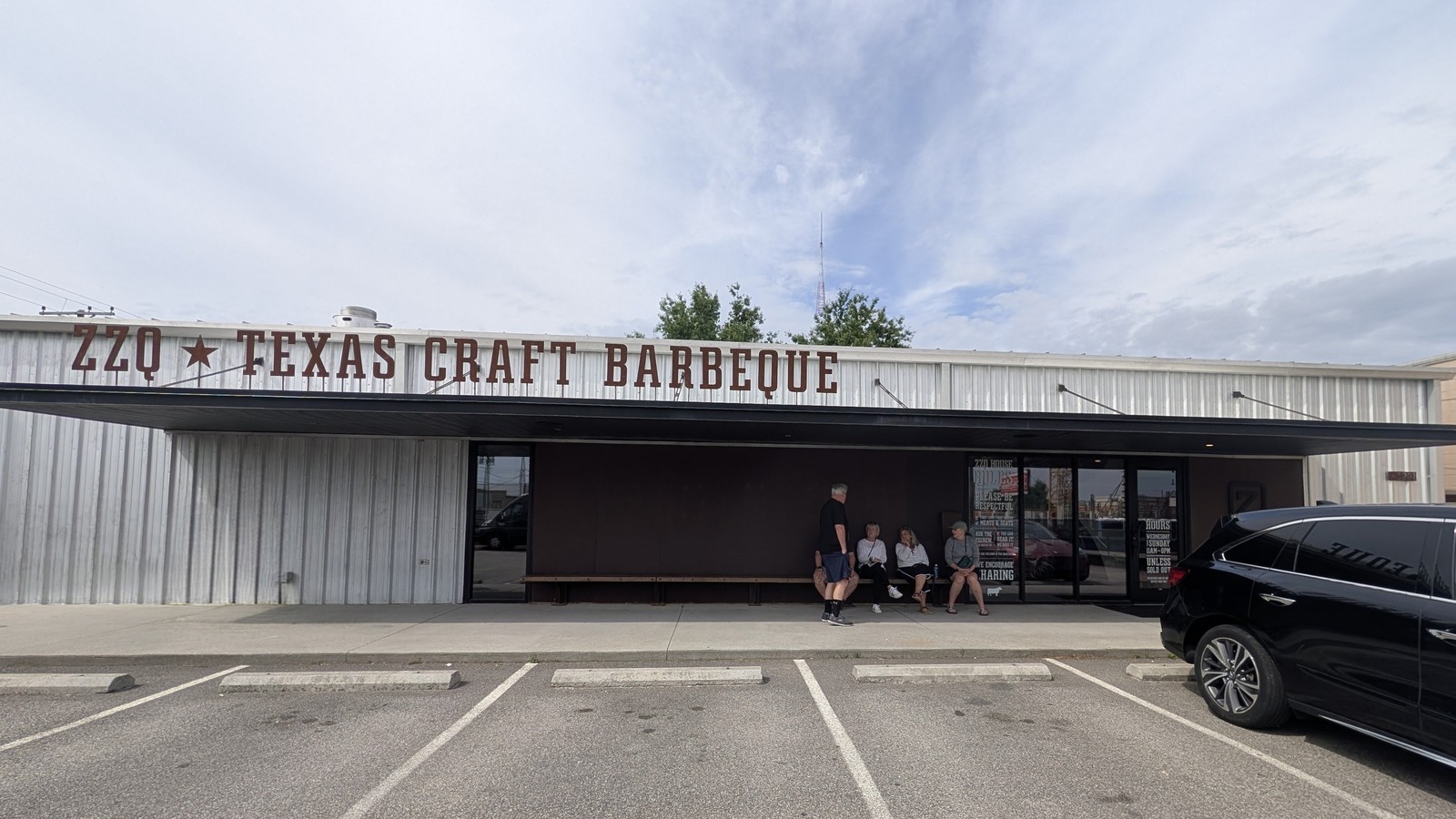 Wide metal-front exterior and shaded entry bench at ZZQ Texas Craft Barbeque in Richmond
