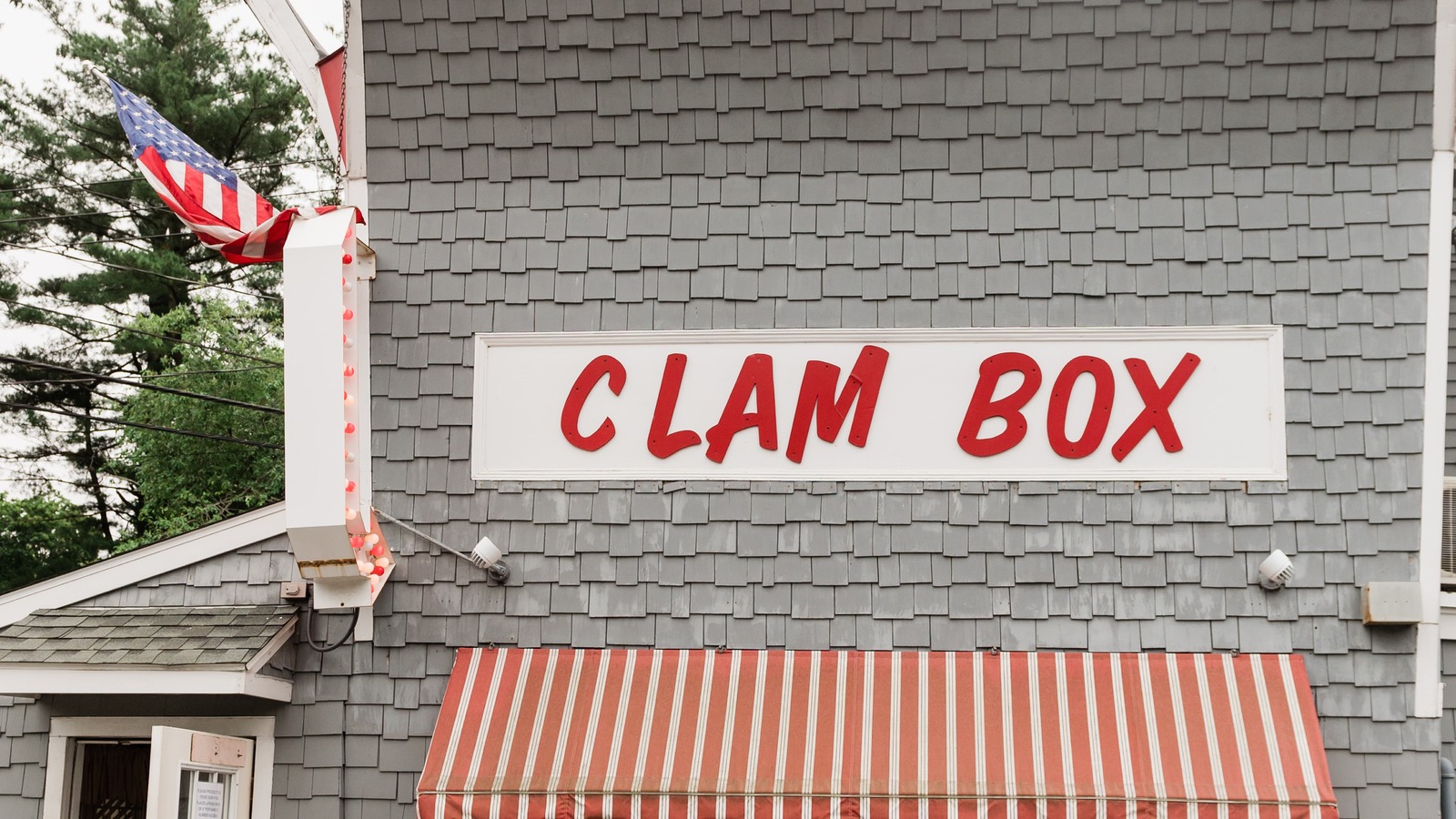 Front facade of the Clam Box with the red-letter sign, striped awning, and bench by the entrance.