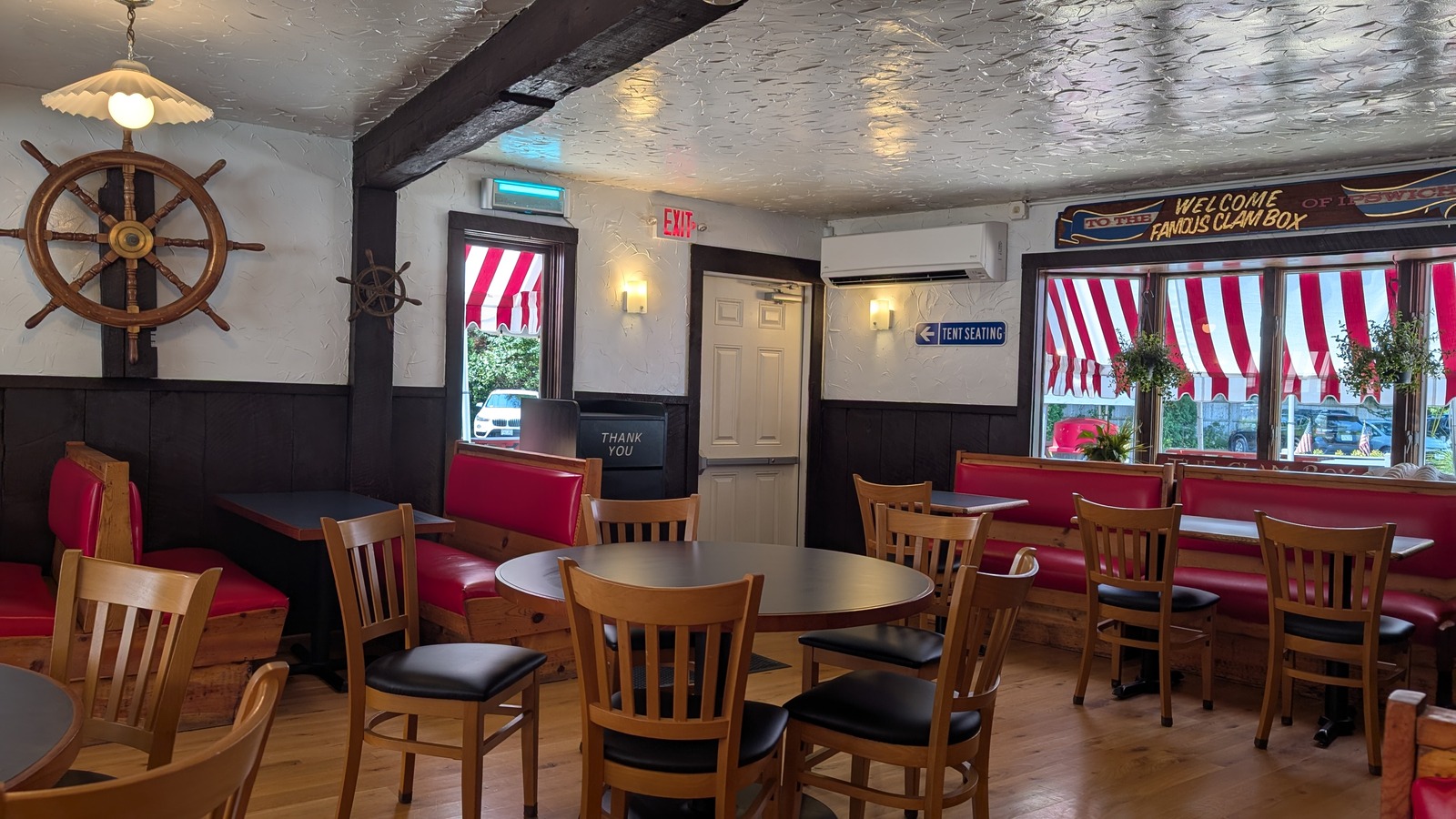 Dining room at the Clam Box with red booths, wood chairs, and a ship wheel on the wall.
