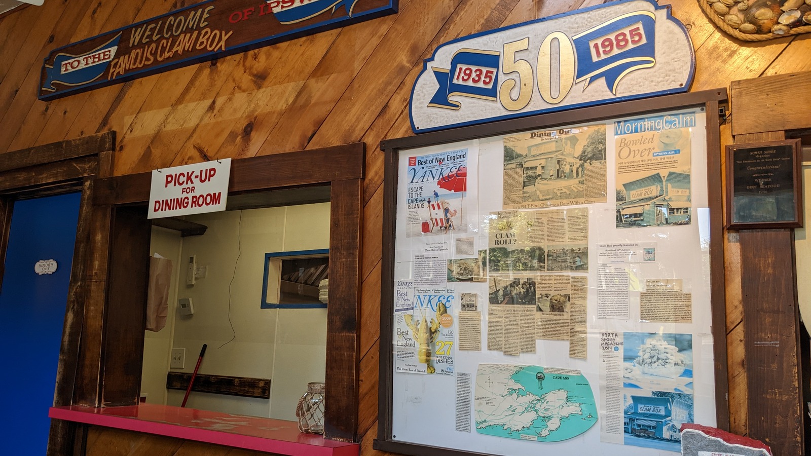 Pickup window and wood-paneled wall filled with Clam Box clippings and anniversary signage.