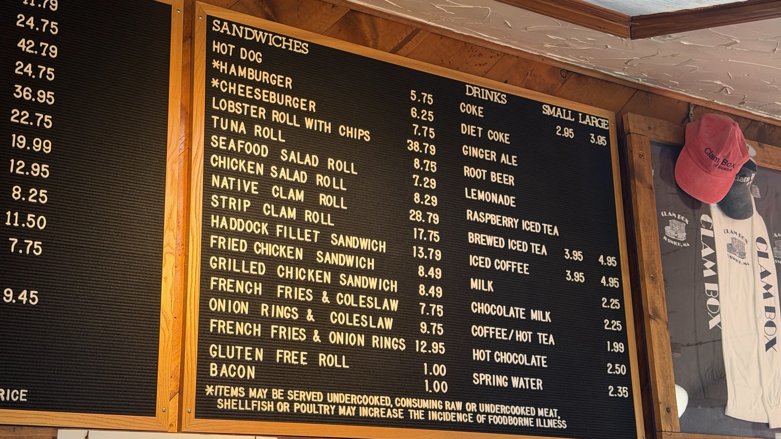 Black menu board at the Clam Box listing seafood plates, sandwiches, and drinks beside hanging merchandise.