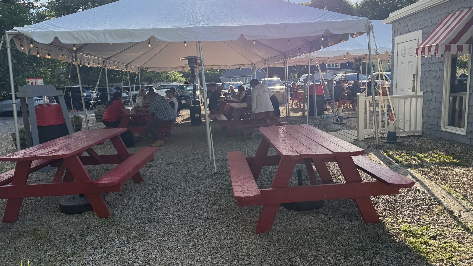 Tent-covered outdoor seating at the Clam Box with red picnic tables on the gravel patio.