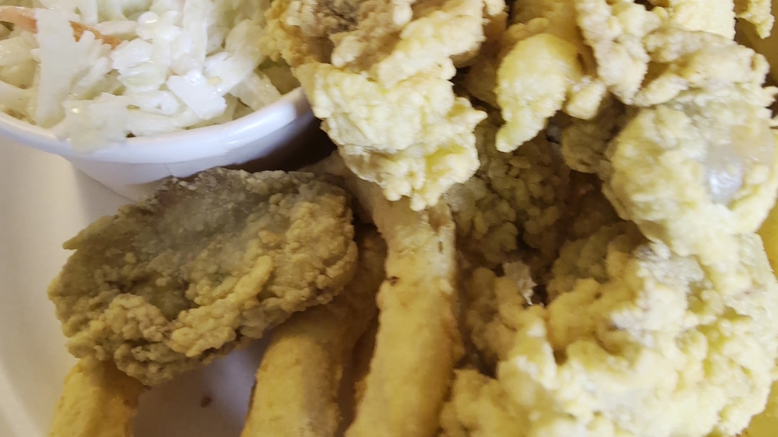Close-up of fried clams, onion rings, fries, and slaw piled onto a paper plate.