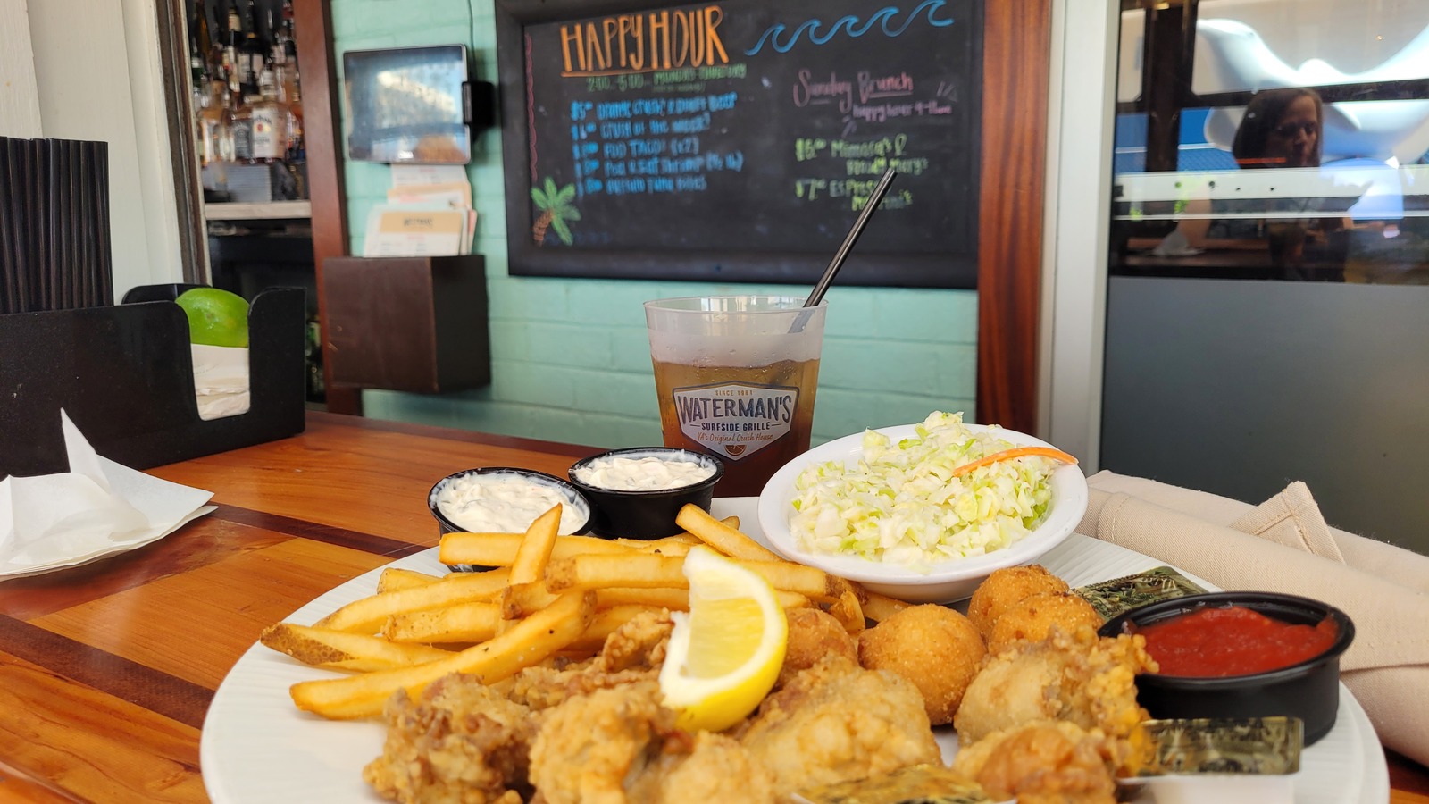 Fried shrimp plate with fries, coleslaw, and sauces at Waterman's Surfside Grille