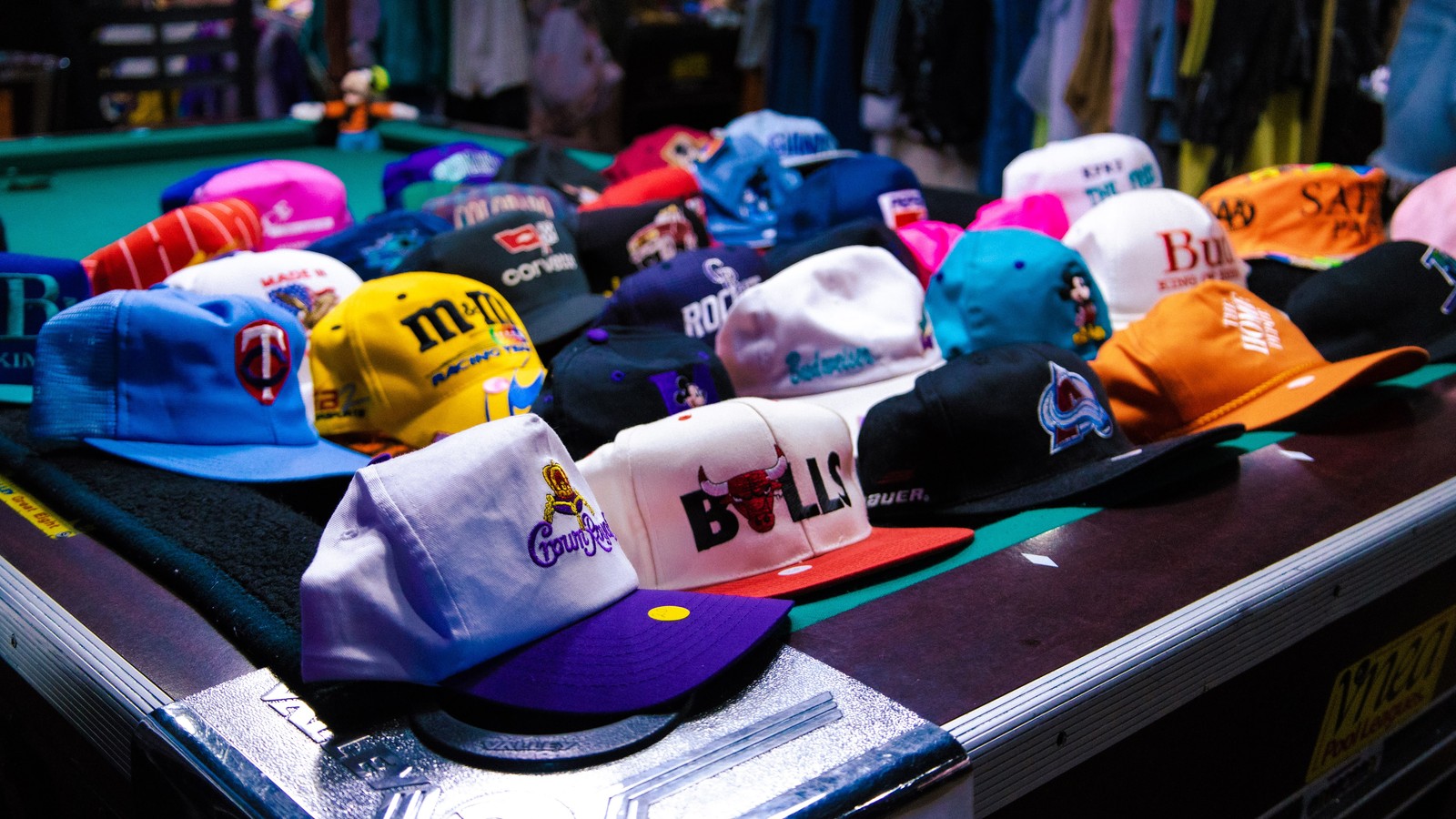 A lineup of colorful vintage caps spread across a pool table inside Collective Vintage in Fort Collins