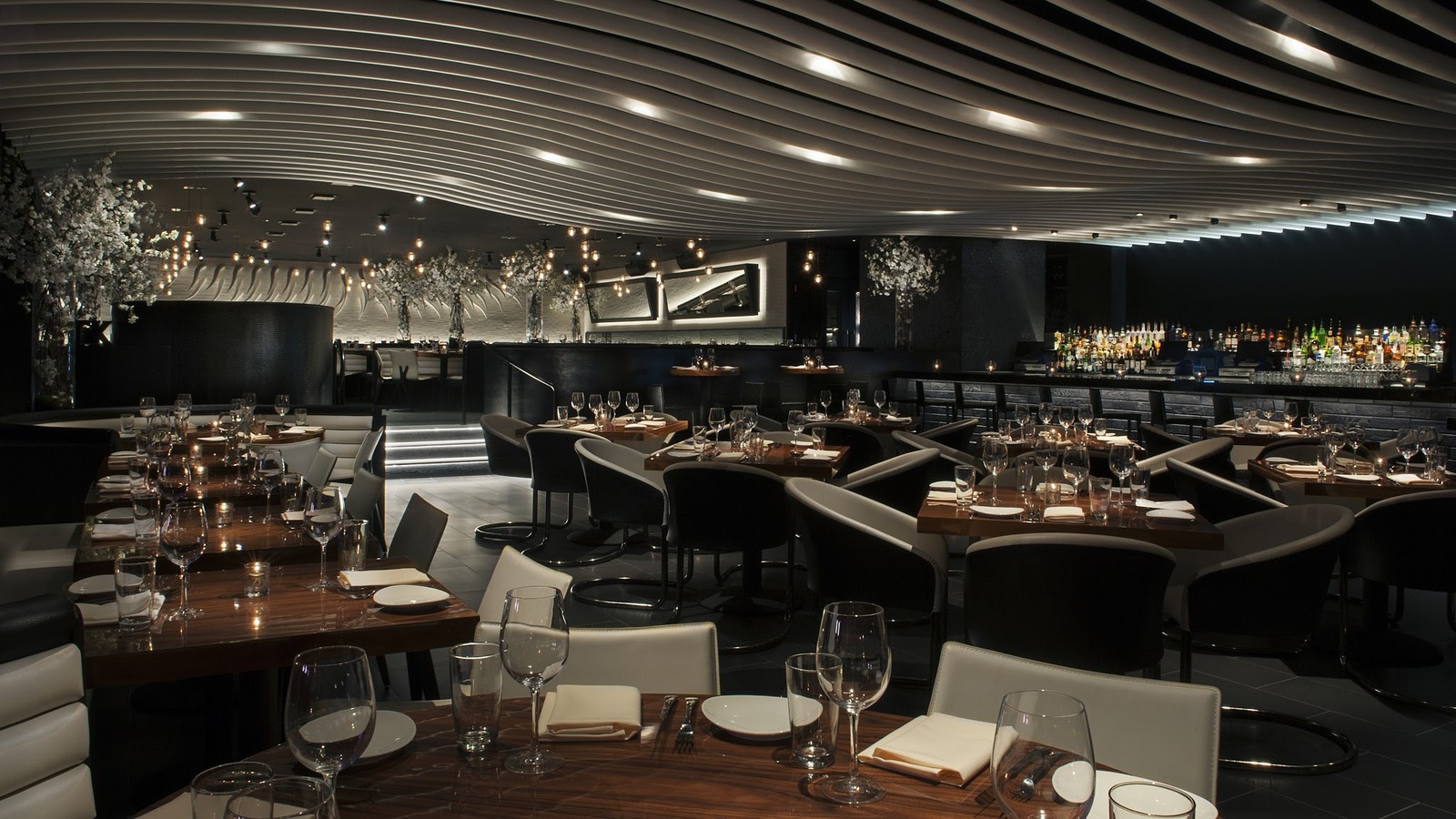 Dim STK dining room in Orlando with sweeping ceiling panels, candlelit tables, and a glowing bar