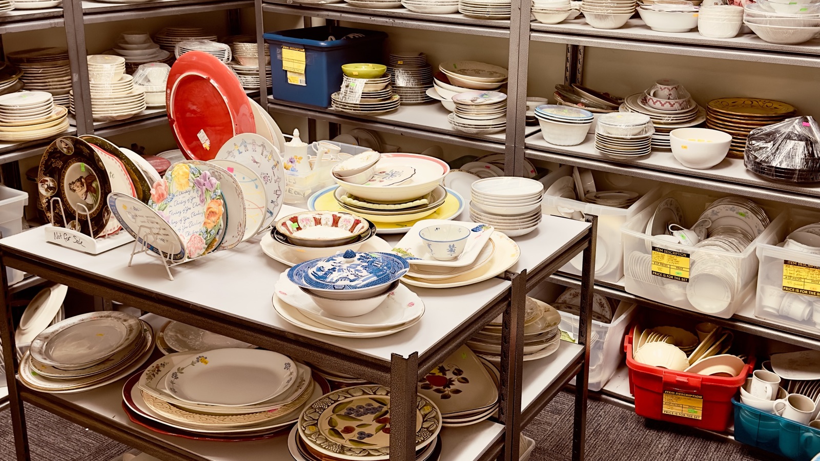 Shelves and tables filled with plates, bowls, and serving pieces at New Life Thrift