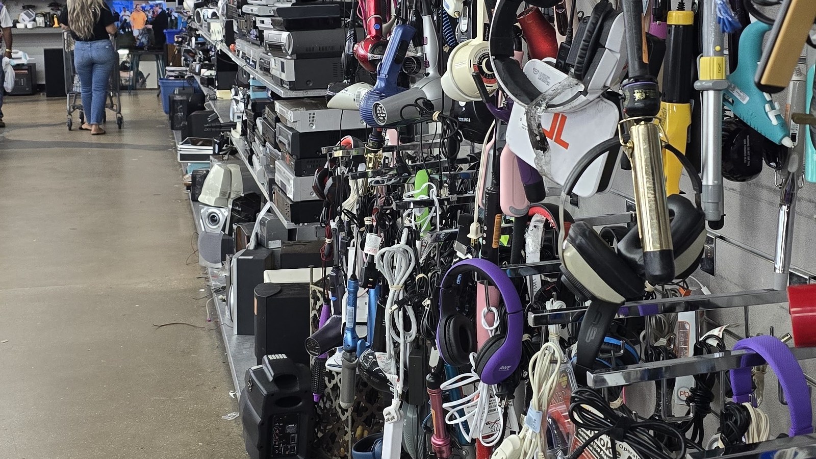 Vacuums, headphones, and household electronics arranged along a Hialeah thrift aisle