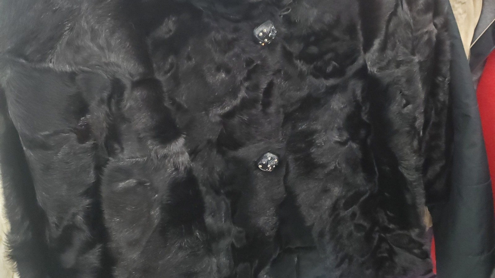 Black faux-fur coat with a jeweled button on an apparel rack