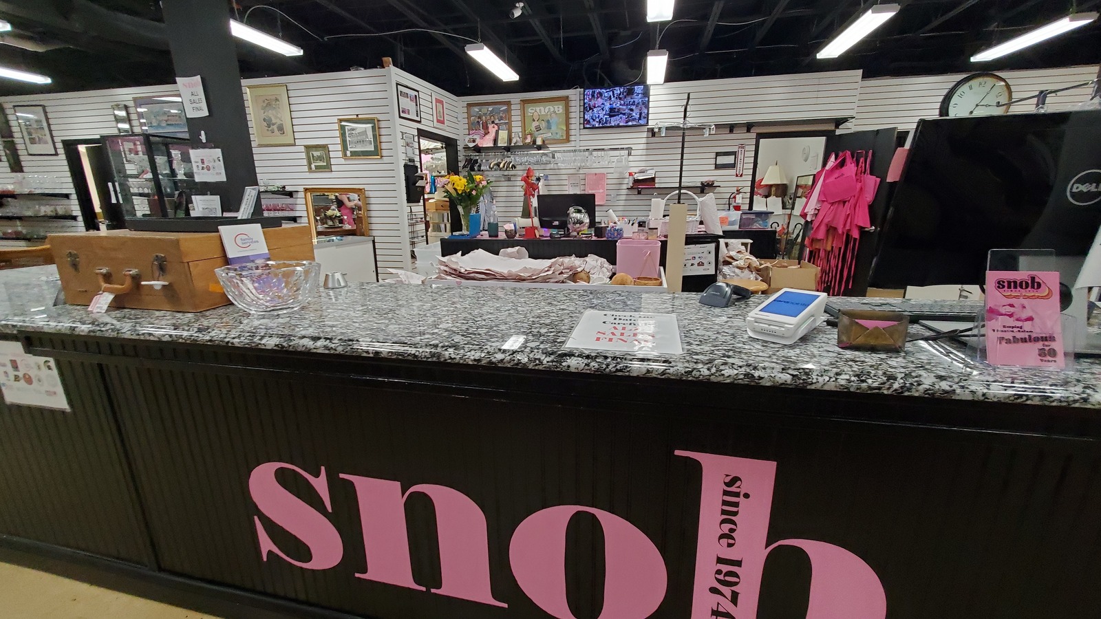 A black counter with pink Snob Shop lettering surrounded by vintage furniture and framed art in Winston-Salem