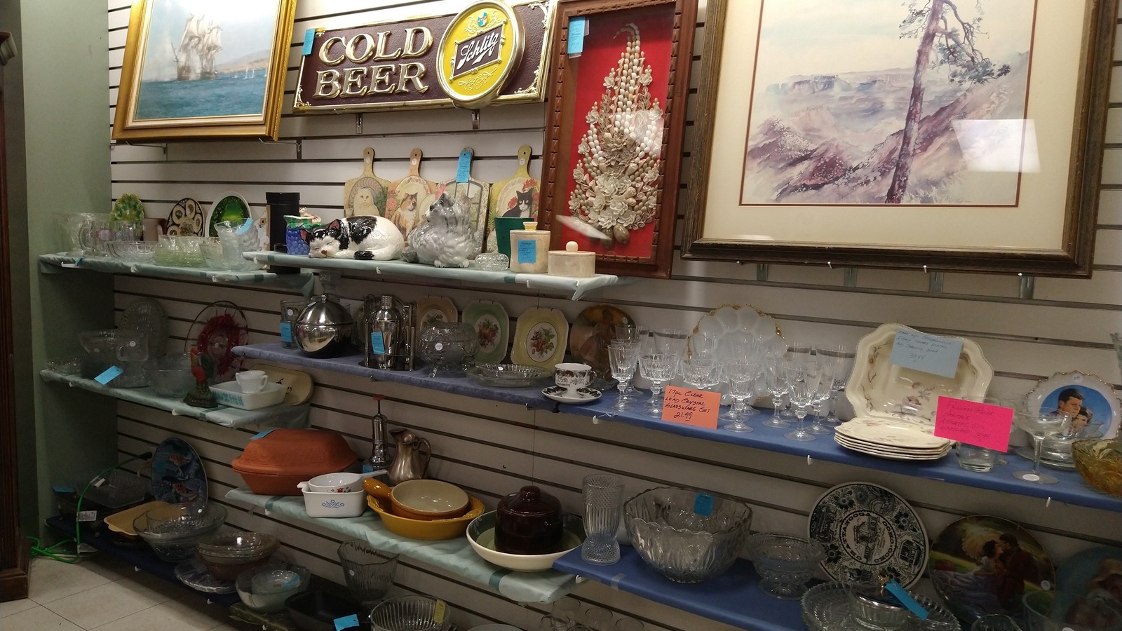 Framed art, pottery, glassware, and vintage decor on a display shelf