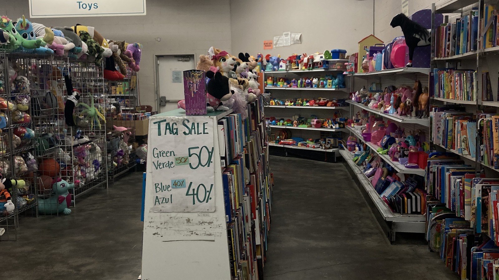 Toy department with plush animals, books, dolls, and a color-tag sale sign