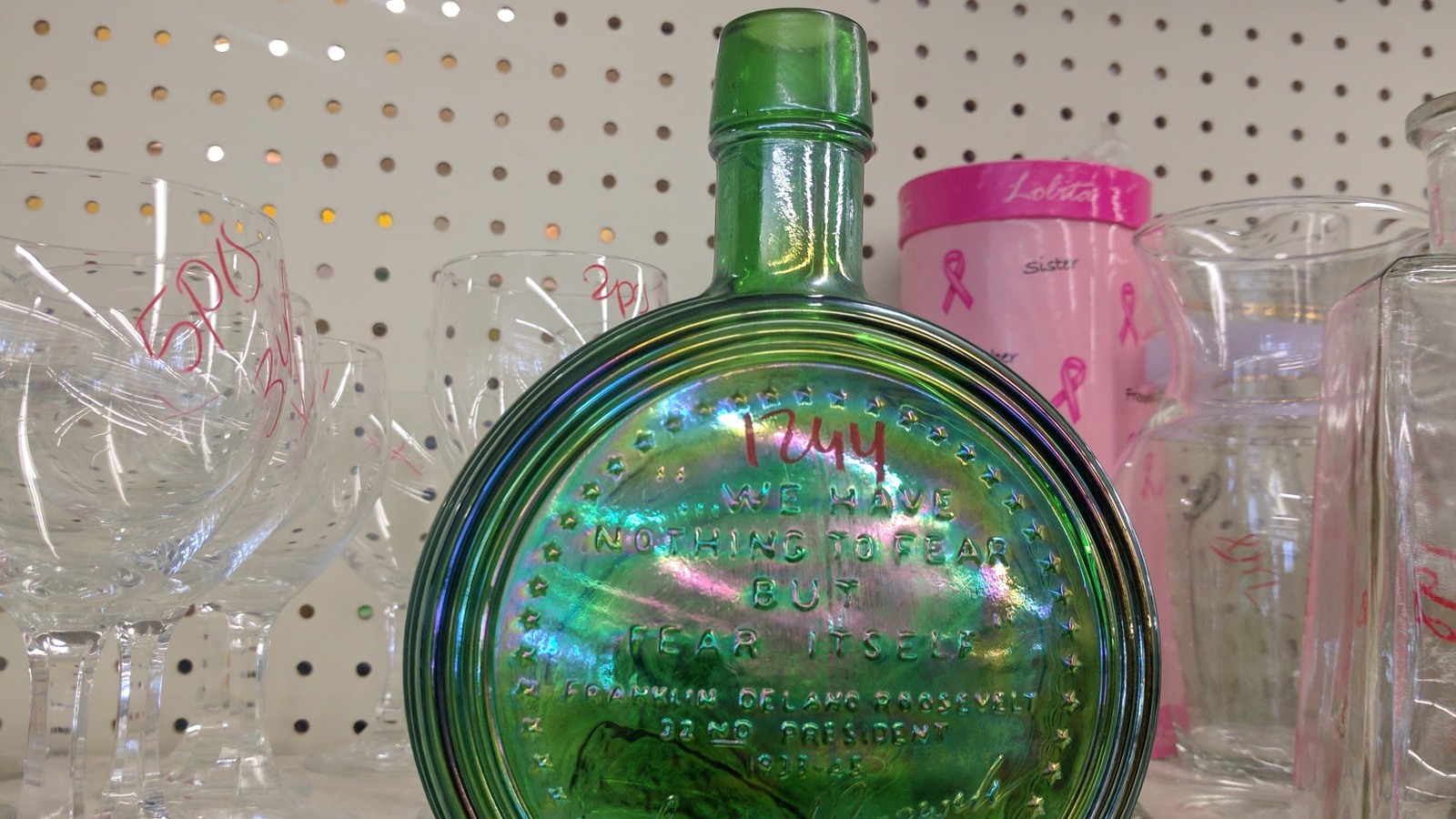 Green iridescent bottle surrounded by clear and pink glassware