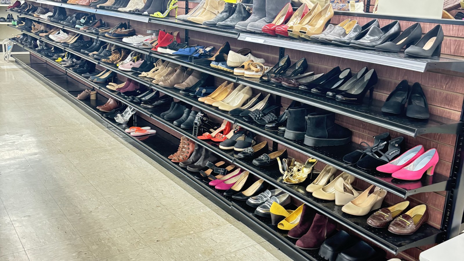 Long wall of secondhand shoes organized on black shelves