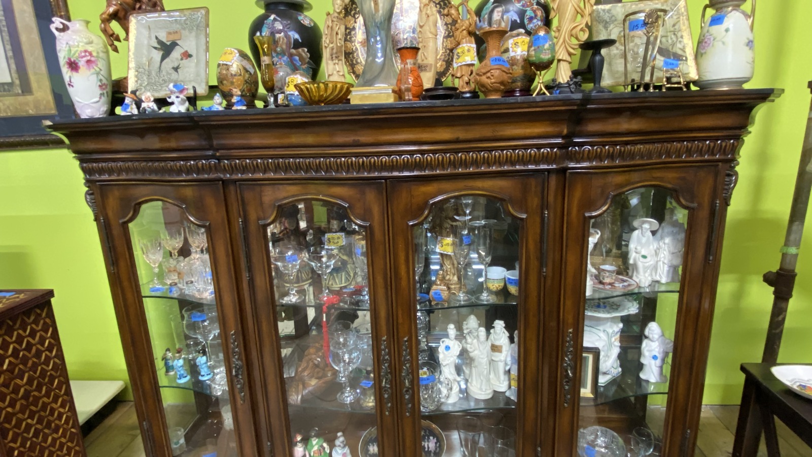 Antique figurines and glassware displayed inside a wooden cabinet at J&B Antiques in Gastonia