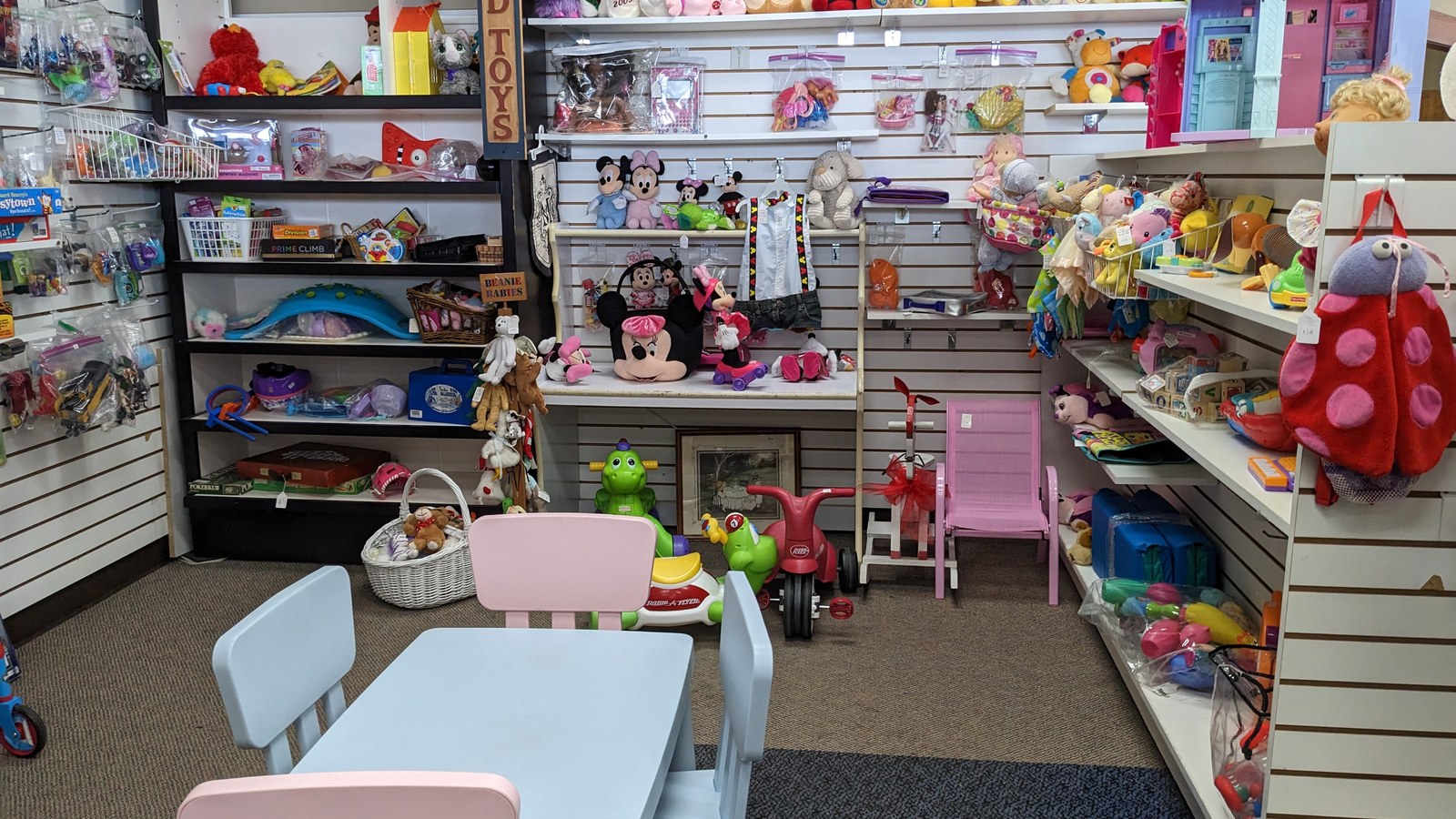 Colorful toys, dolls, and a child-sized table arranged on store shelves