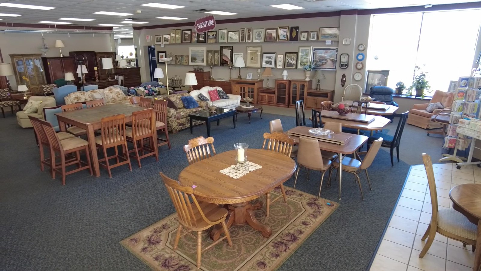 Dining tables, chairs, and framed art across a sunlit furniture room