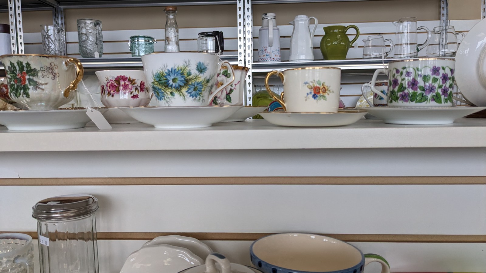 Floral dishes, serving pieces, and glassware arranged on white shelves