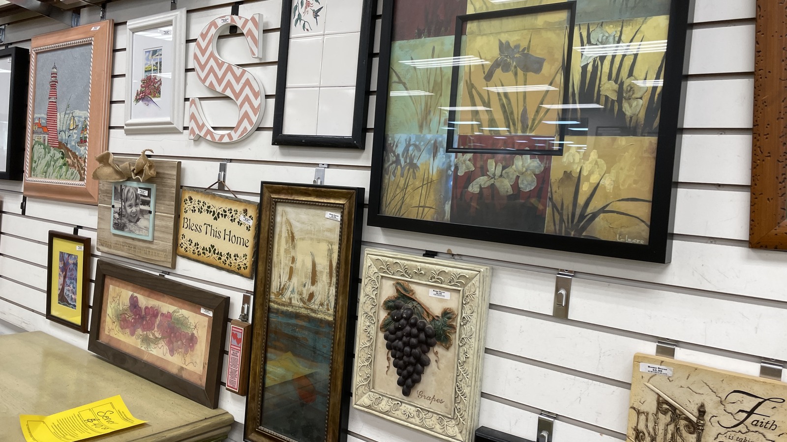 Framed landscapes, floral art, and decorative prints on a display wall
