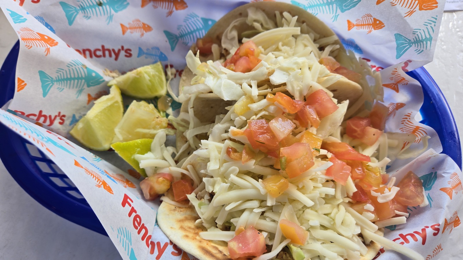 Close view of fish tacos with cabbage, cheese, tomato, and lime wedges at Frenchy's