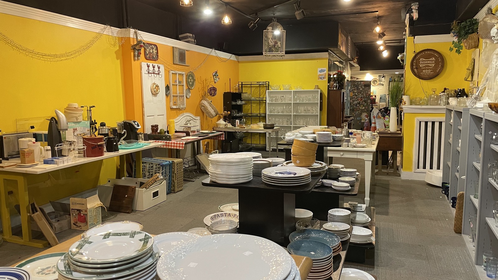 Yellow-walled housewares aisle filled with dishes and shelves at Philly AIDS Thrift in Philadelphia