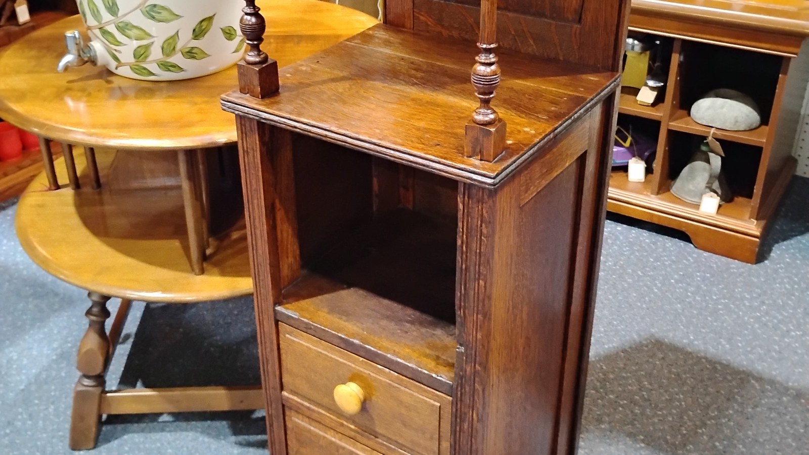 Wooden antique stand beside a crock, round table, and shelves of household pieces at Exit 76 Antique Mall
