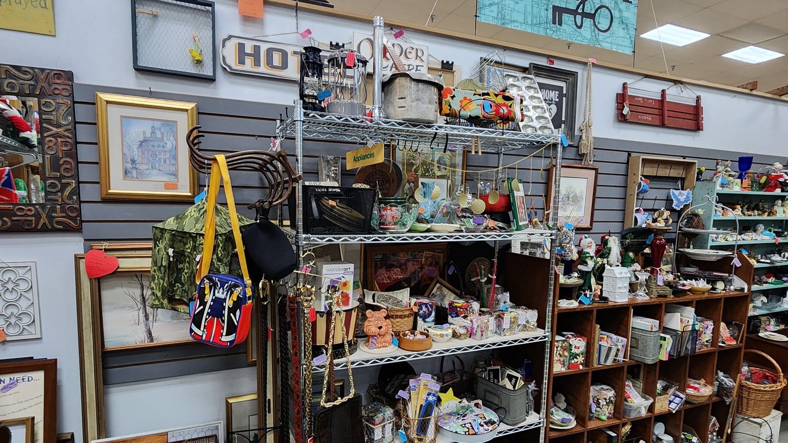 Mixed-decor booth with framed art, hanging signs, shelves, and small collectibles inside Vintage Treasures Antique Mall