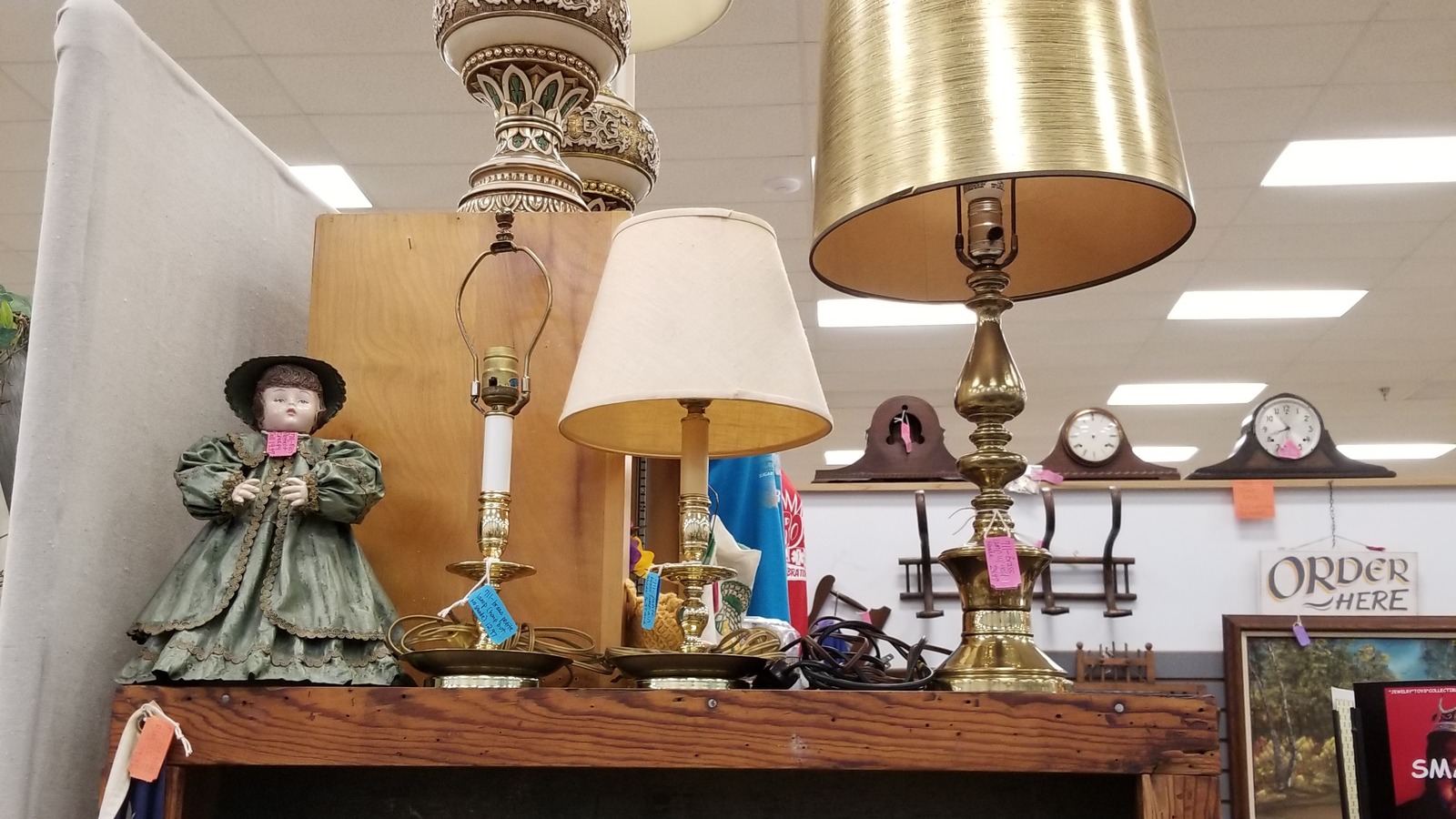 Vintage table lamps, mantel clocks, and a porcelain doll on a display shelf at Vintage Treasures Antique Mall