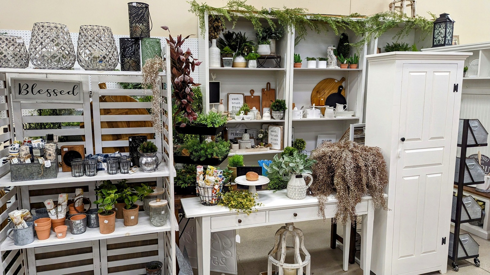 Bright white decor booth with greenery, shelves, and home accents at Vintage Treasures Antique Mall in Fort Wayne