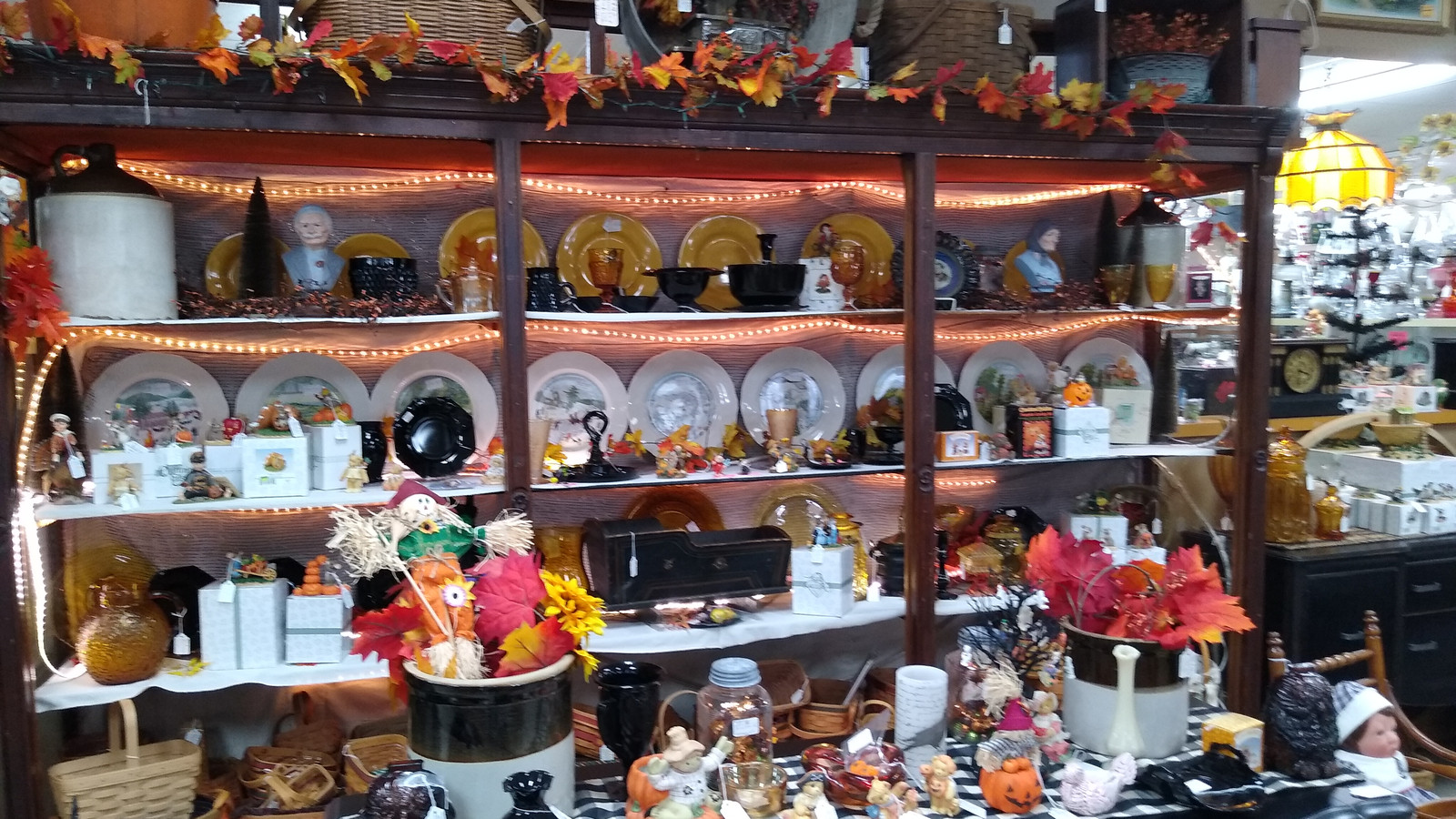 Lit display shelf with autumn decor, amber dishes, and vintage serving pieces at Markle Exit 286 Antique Mall