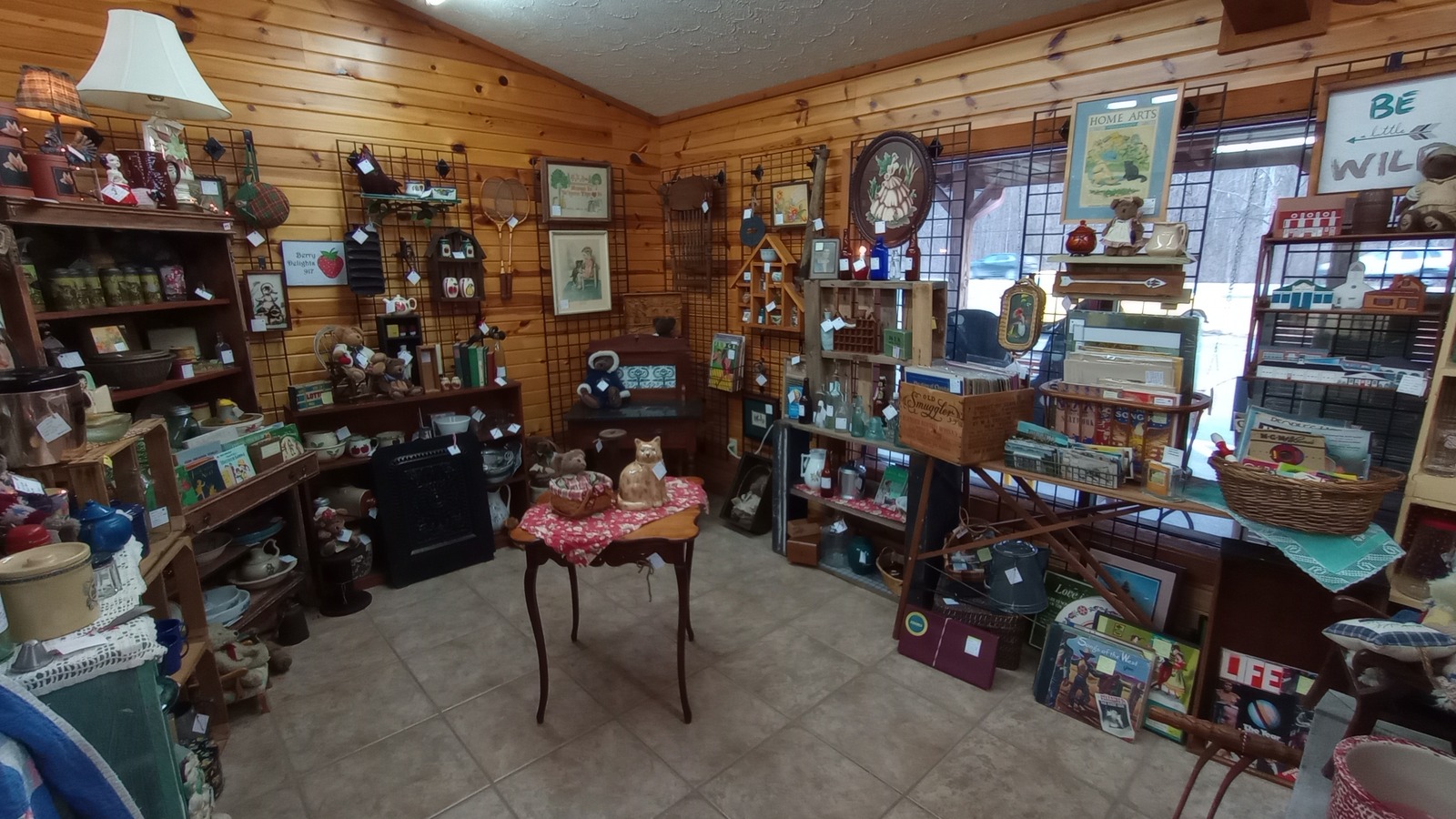 Wood-paneled display room filled with shelves, framed art, pottery, and small antiques at Brown County Antique Mall