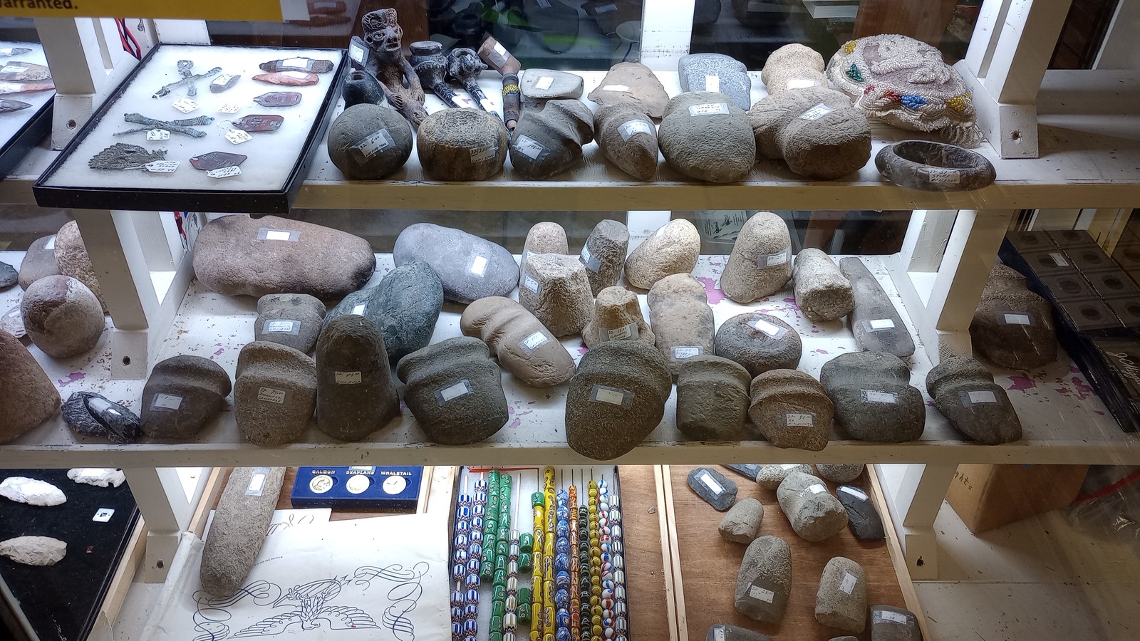 Glass case filled with geodes, carved artifacts, stone pieces, and colorful bead strands at Brown County Antique Mall